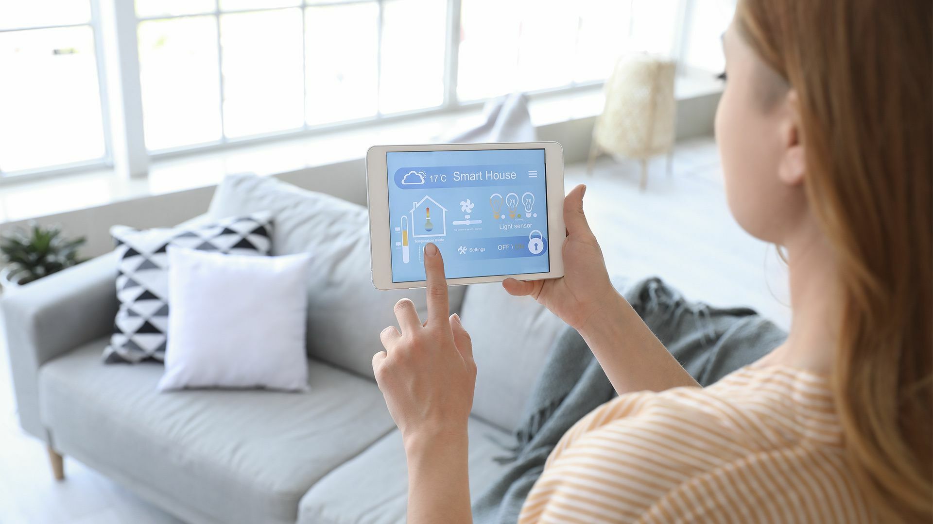 Eine Frau hält einen Tablet-Computer mit einer Smart Home Anwendung im Wohnzimmer